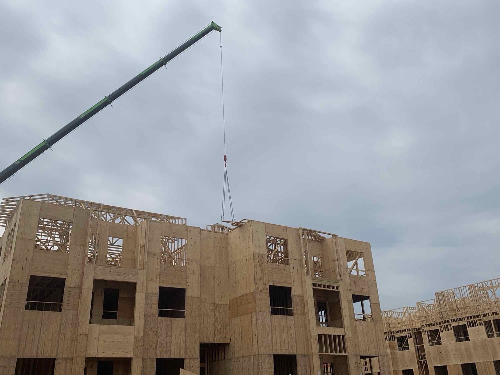 Crane lifting a framed wall panel into place on a multi-story building